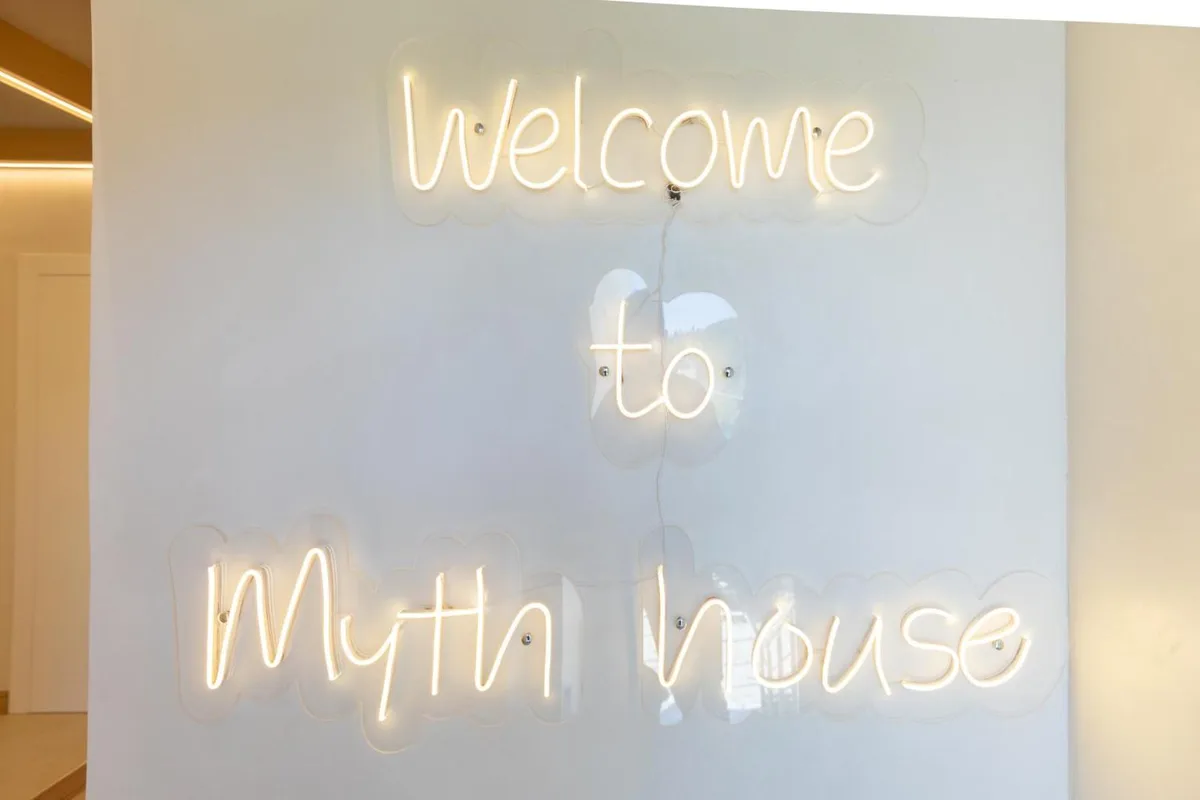 A warm-white neon script on the wall inside Dimitri Hotel reading Welcome to Myth house
