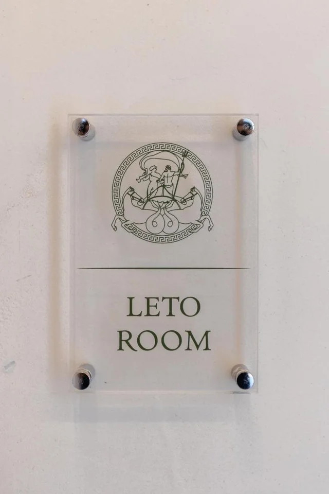 An etched acrylic door plate at Dimitri Hotel, held off the wall on four steel bosses, carrying the green crest above the words LETO ROOM
