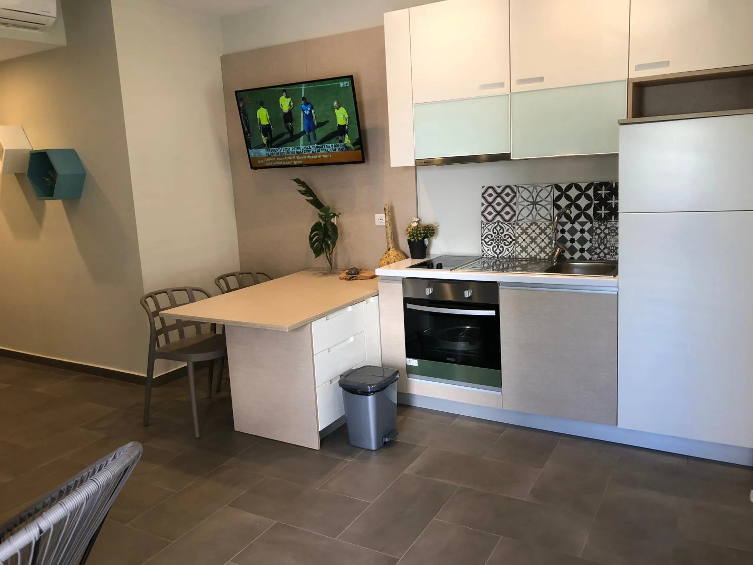 A white kitchen with an oven, a hob, patterned tiles behind the counter and a small dining table