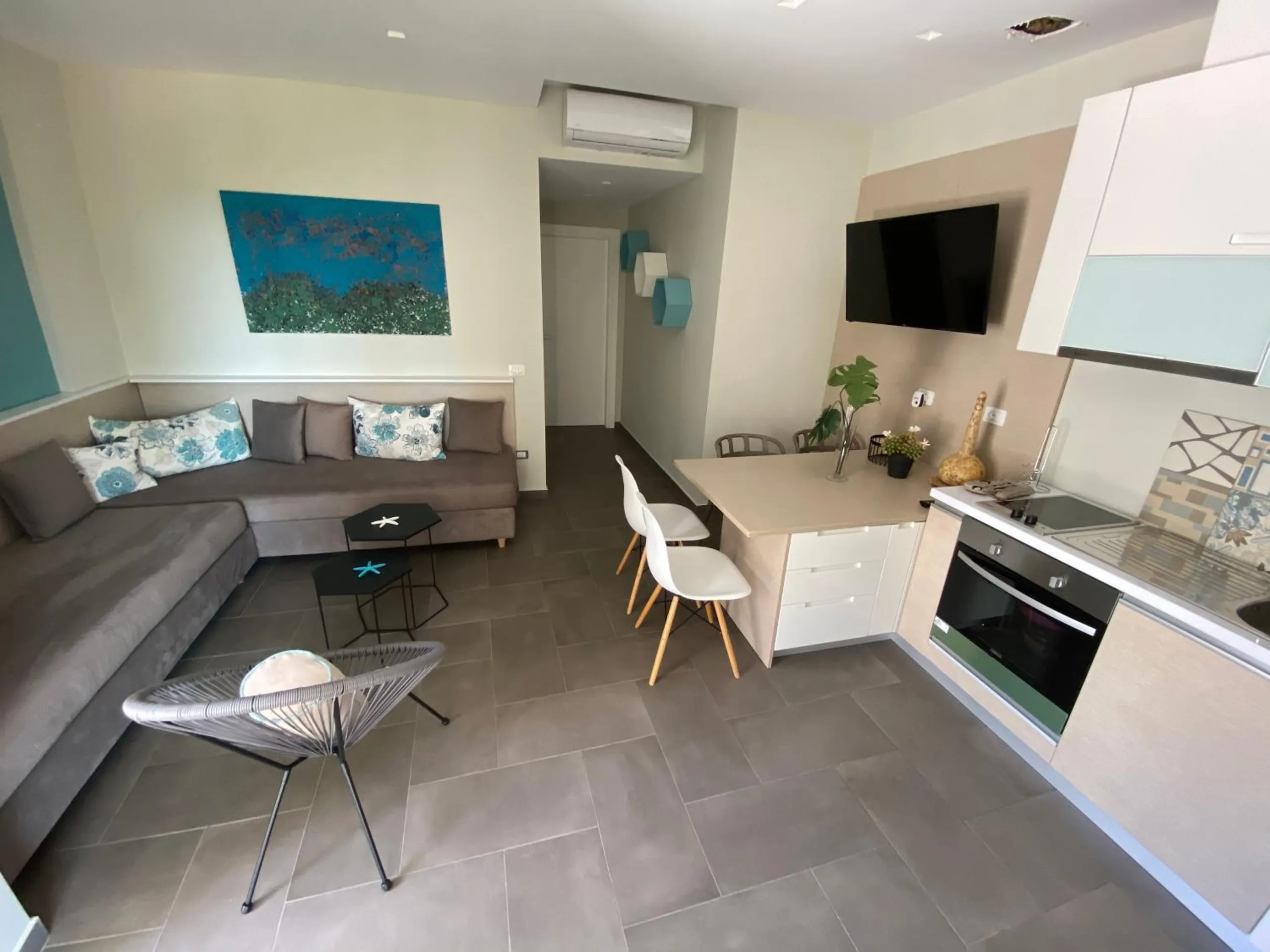 An open-plan room with a corner sofa, a dining counter with white chairs and a kitchen along the wall