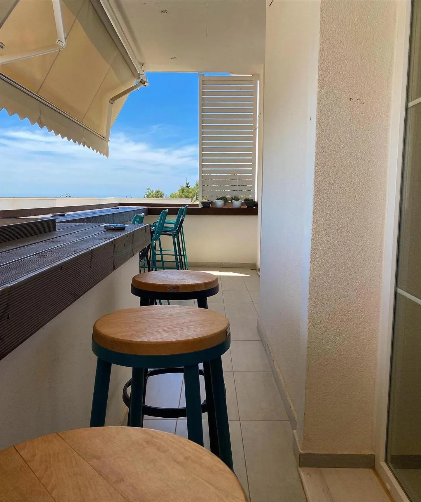 Round wooden stools along a dark timber counter, the sea and a low headland beyond