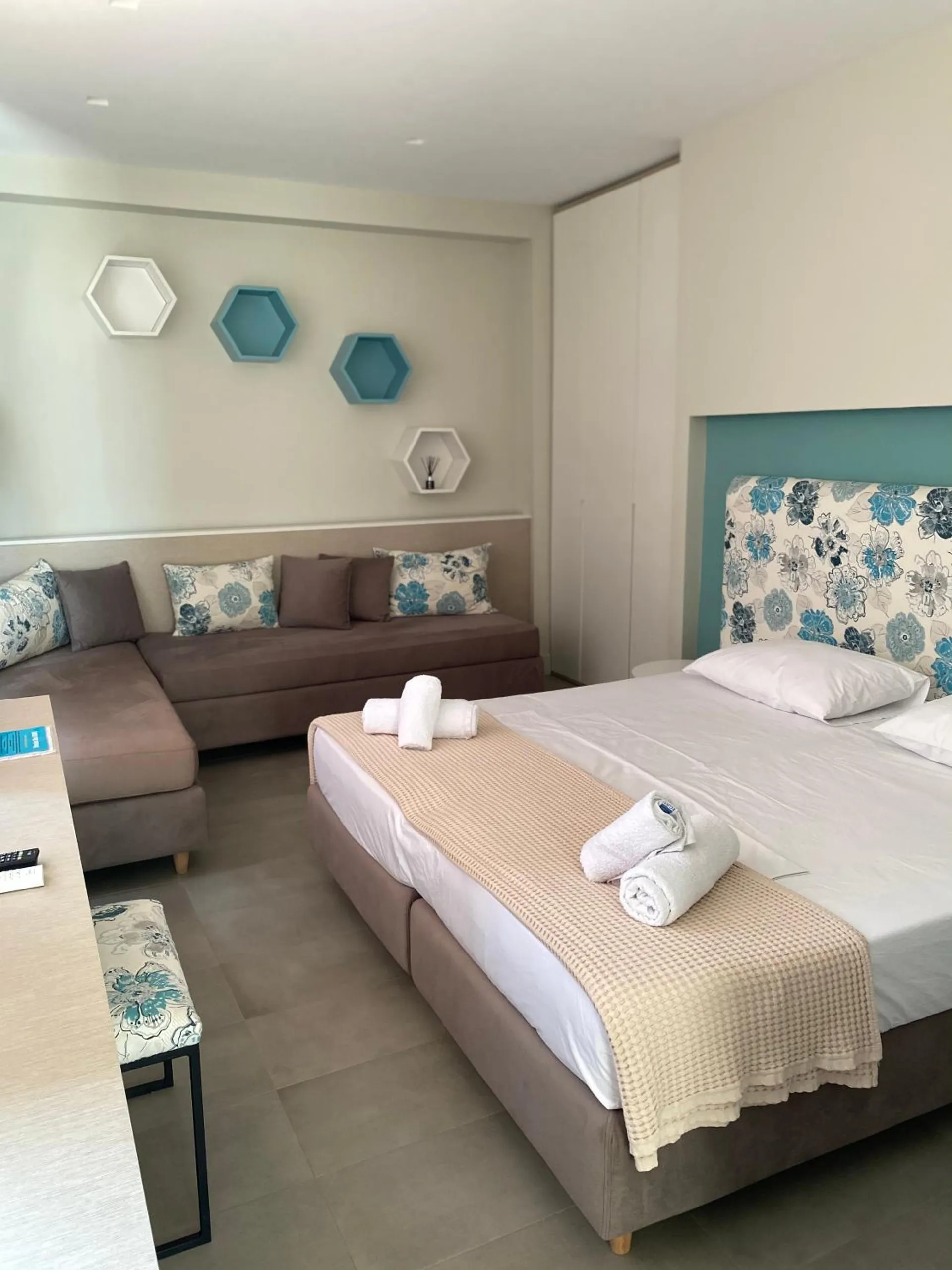 A bed with rolled towels and a sofa with flowered cushions under teal hexagon shelves