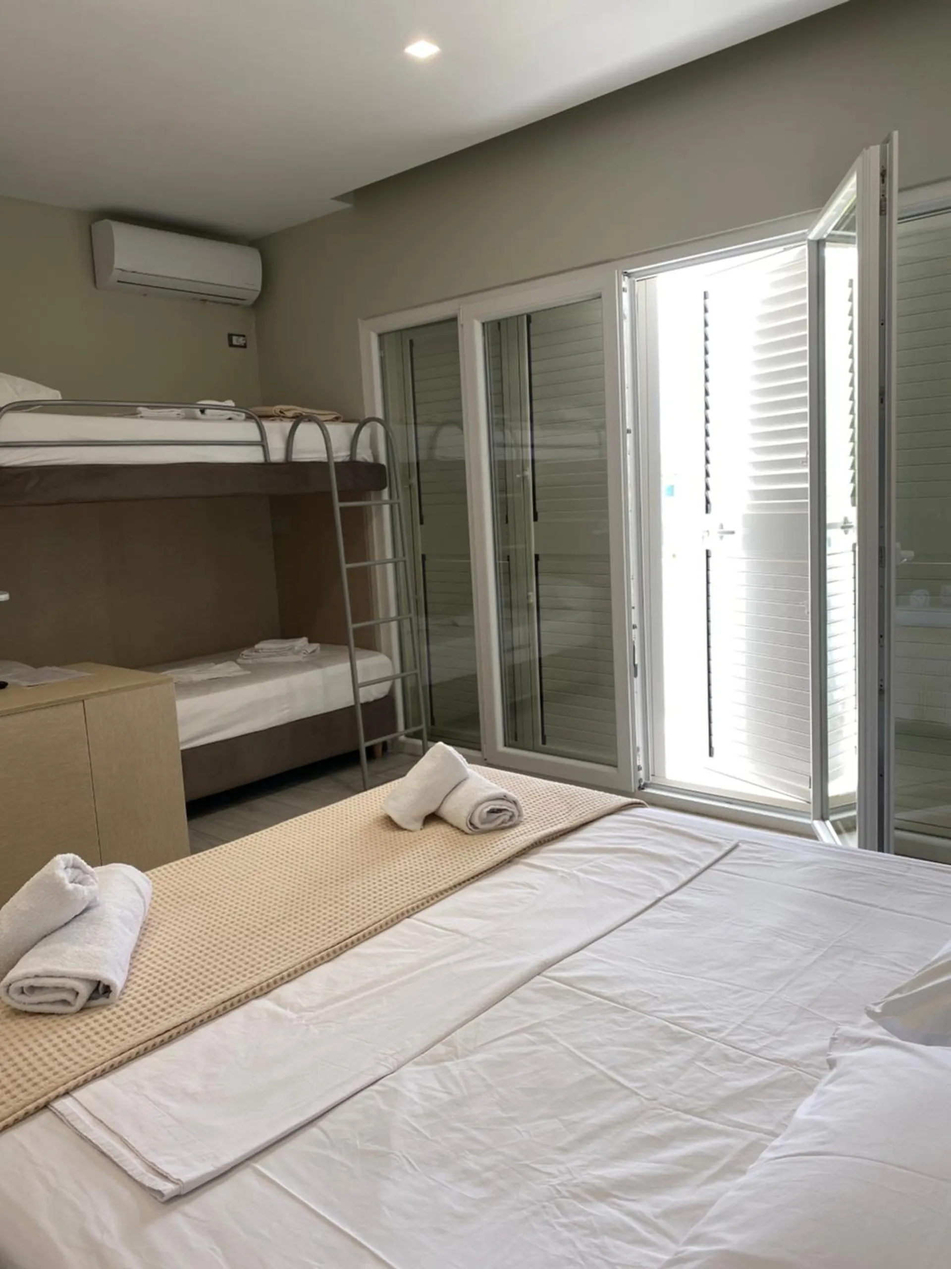 A room with a queen bed and a set of bunk beds beside tall white louvred doors