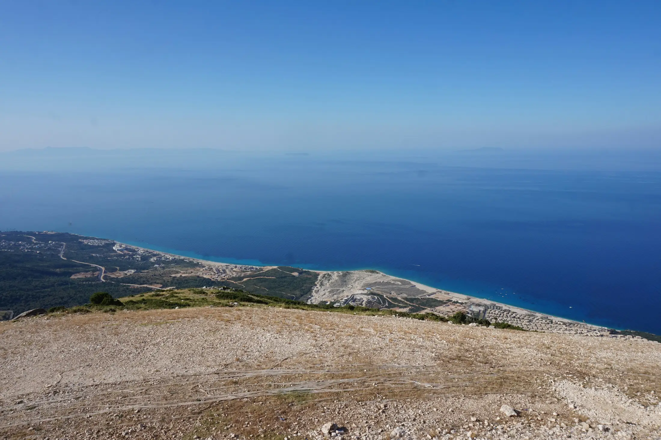The coast seen from high on the mountain: a long pale beach, green plain and villages below, the sea deep blue to the horizon