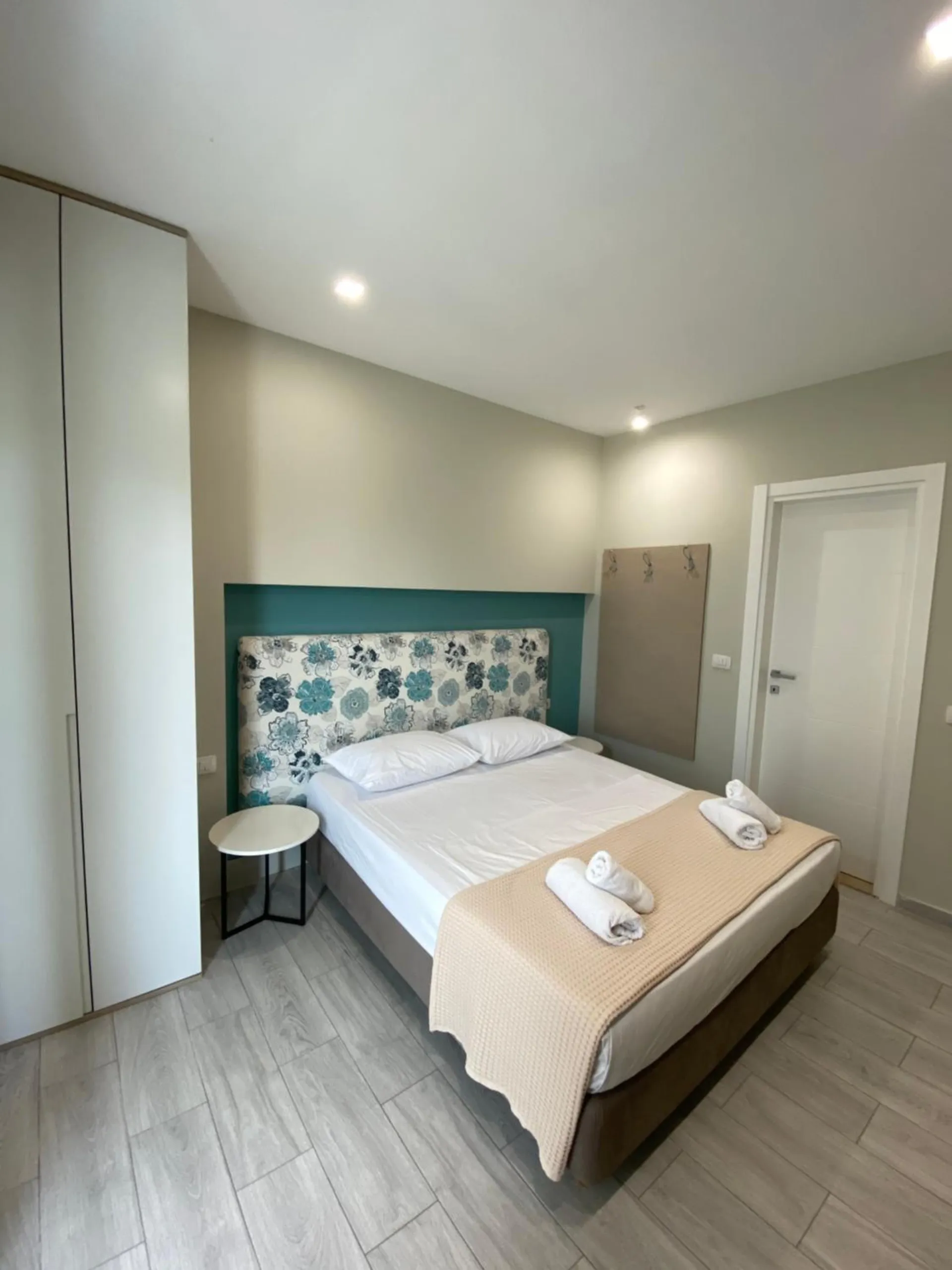 A double bed made in white with a flowered headboard on a teal wall, a white door beside it