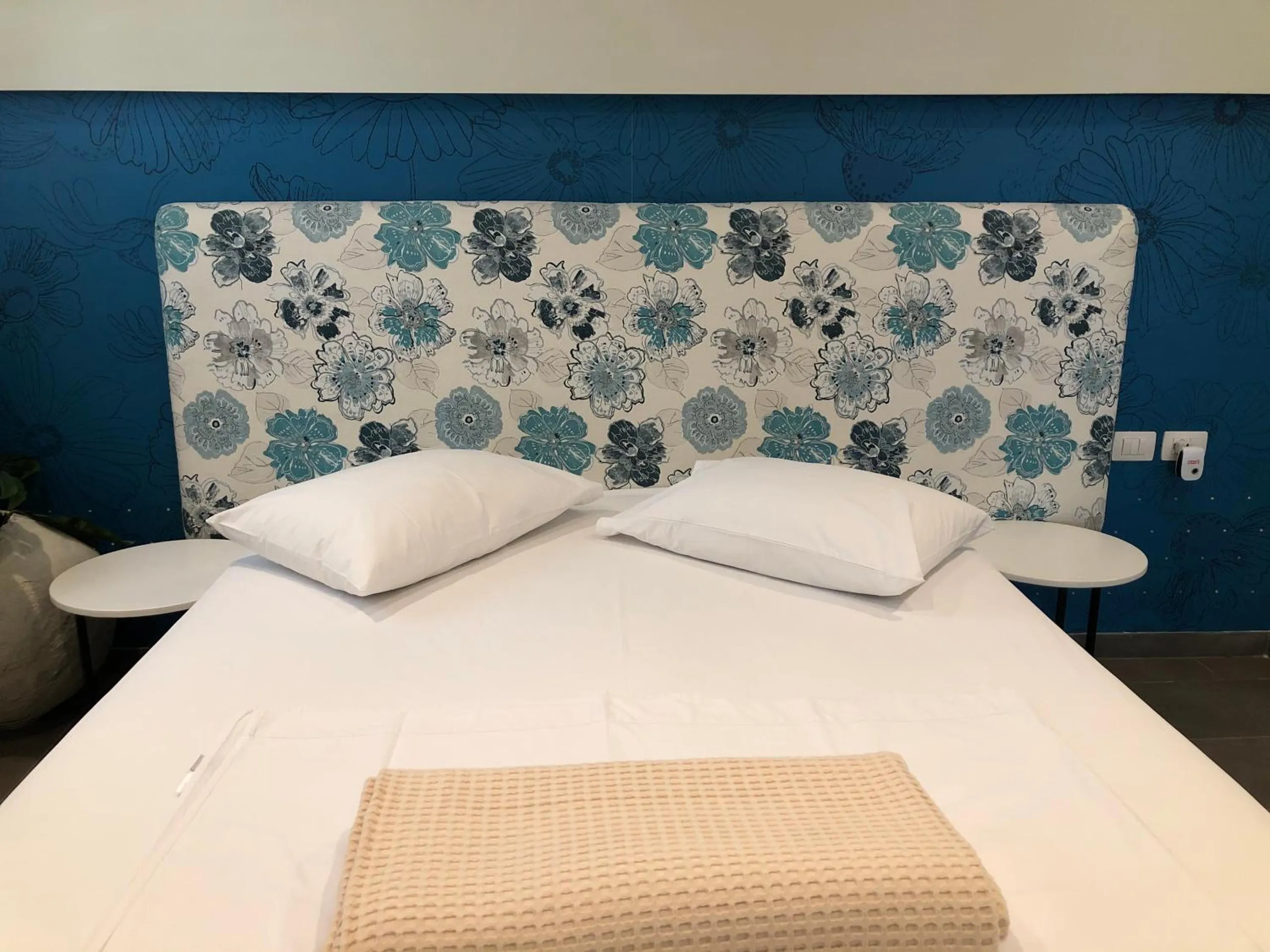 A bed made in white against a deep blue wall, its headboard printed with large blue and teal flowers