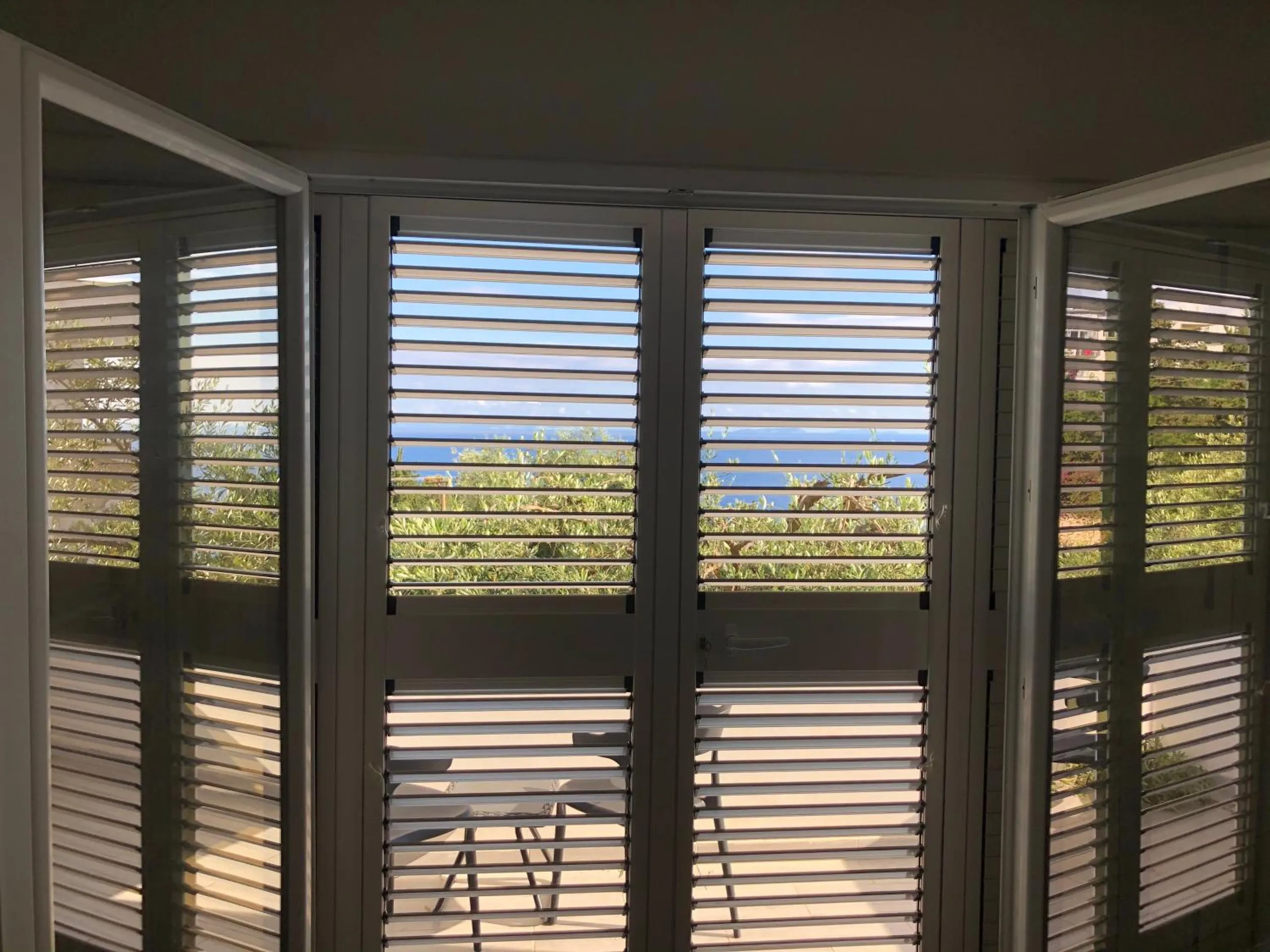 A row of grey louvred doors drawn across a terrace, the sea showing through the slats