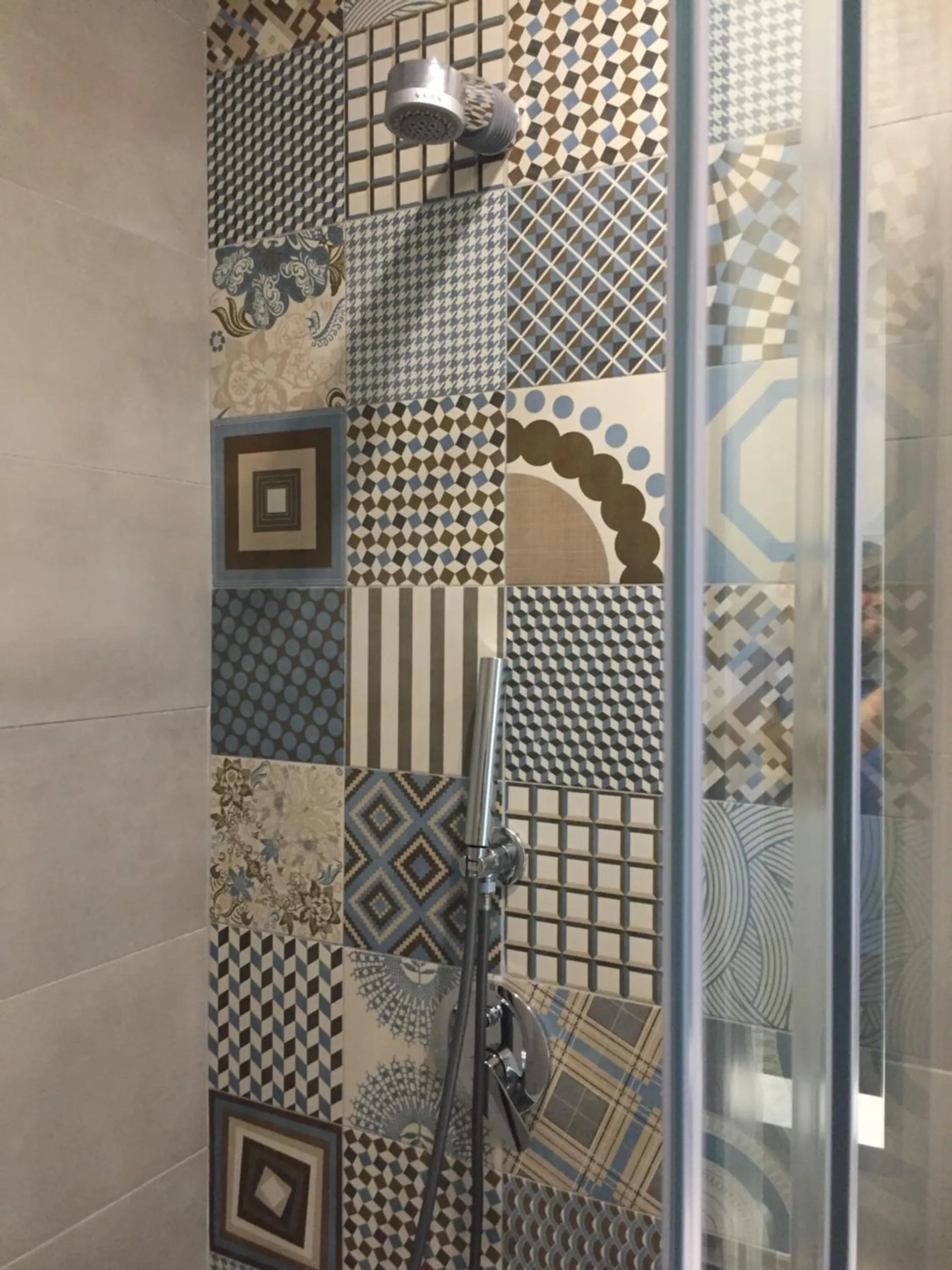 A shower wall of patterned tiles in blue, grey and mustard behind a glass screen