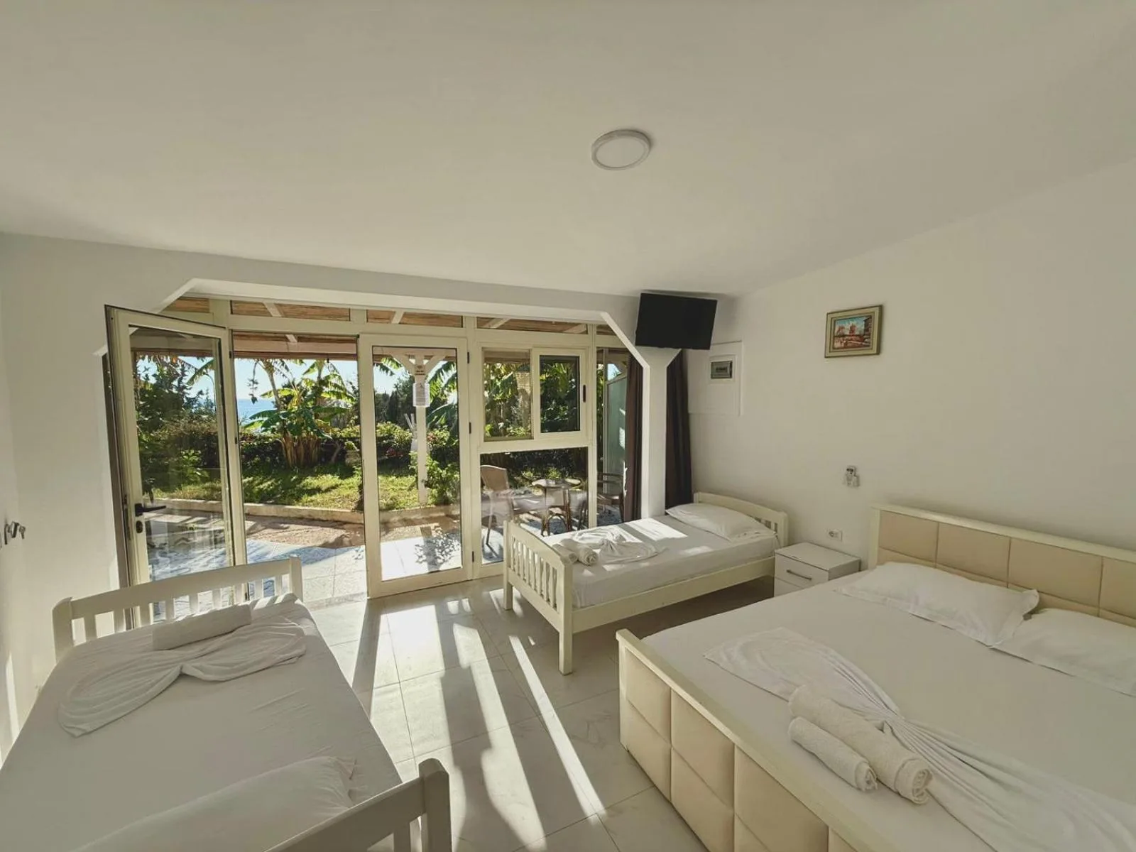 A bright room with a double bed and two single beds on a pale marble-effect floor, its glass doors open onto the veranda and the garden