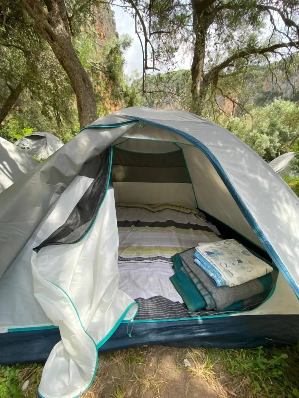 A dome tent with its door unzipped, showing a mattress made up with sheets and a folded stack of bedding and towels inside
