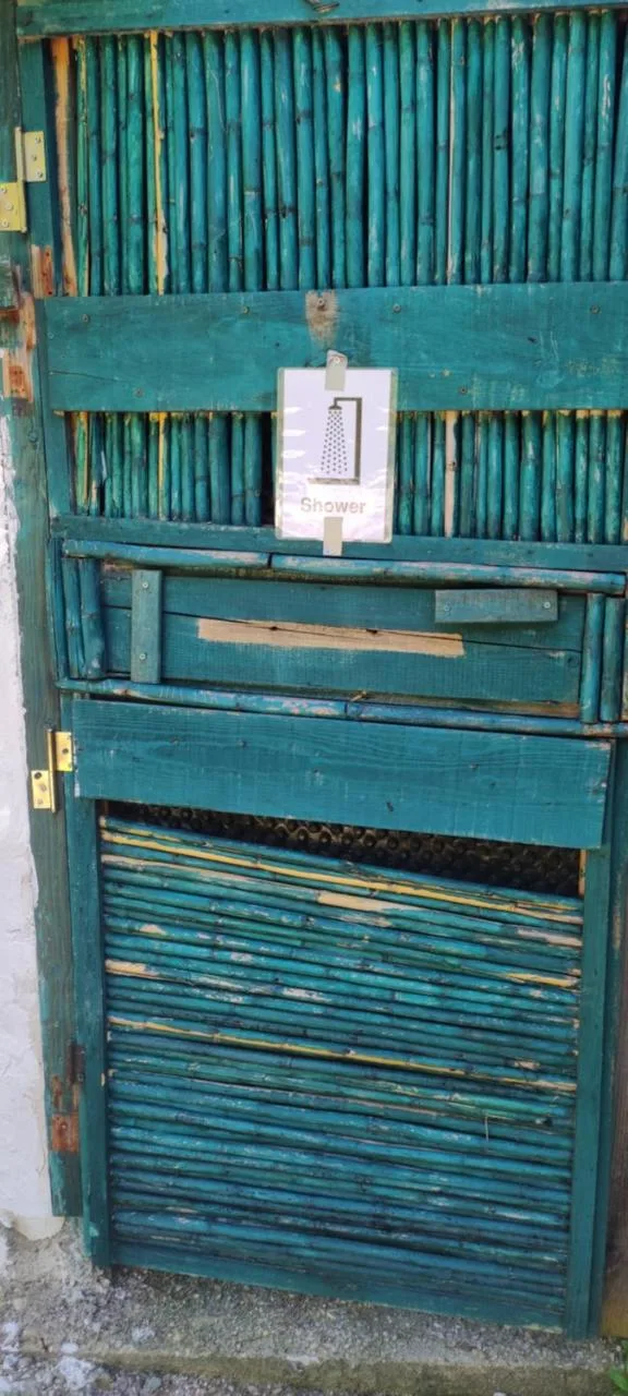 A shower cubicle door made of cane slats painted teal, set in a teal timber frame