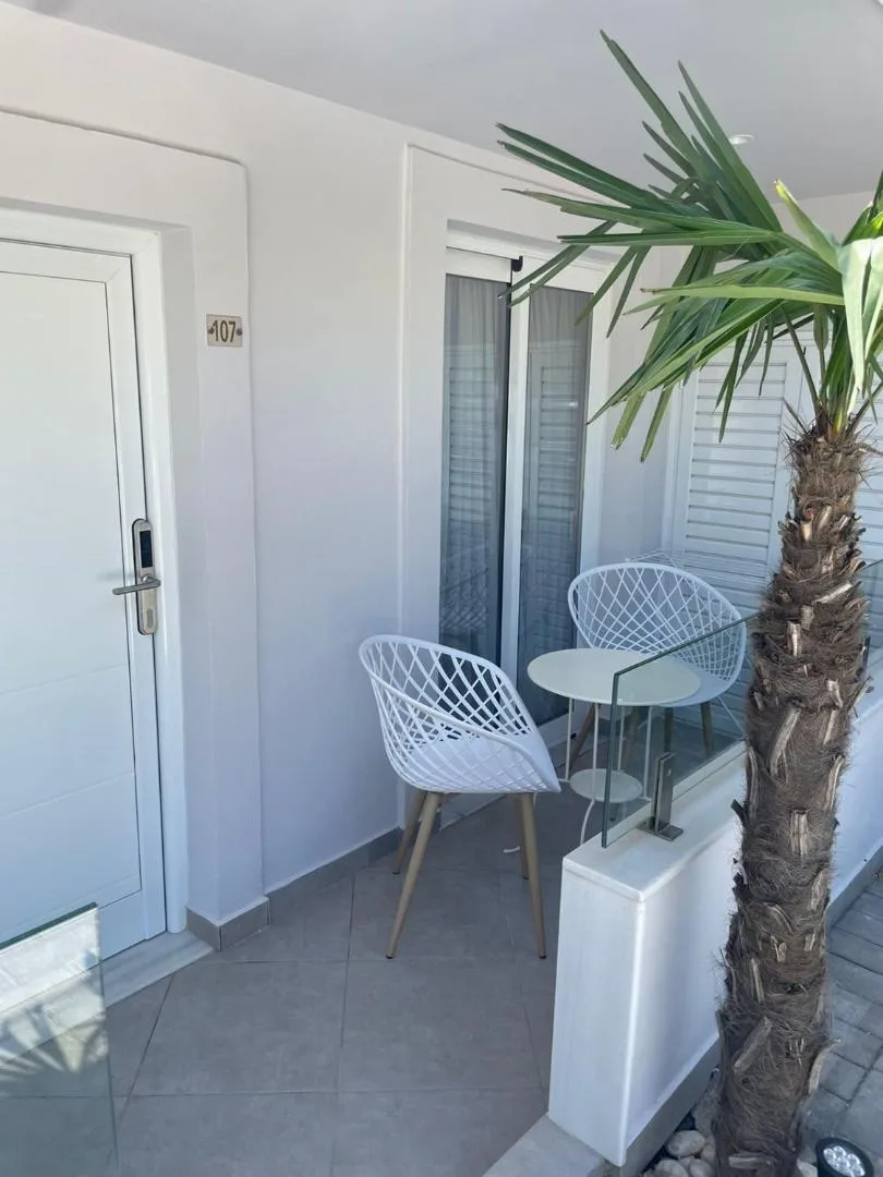 Two white wire chairs and a small table on a room's balcony beside a palm