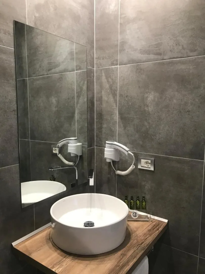 A white vessel basin on a wooden shelf against dark grey stone-effect tiles