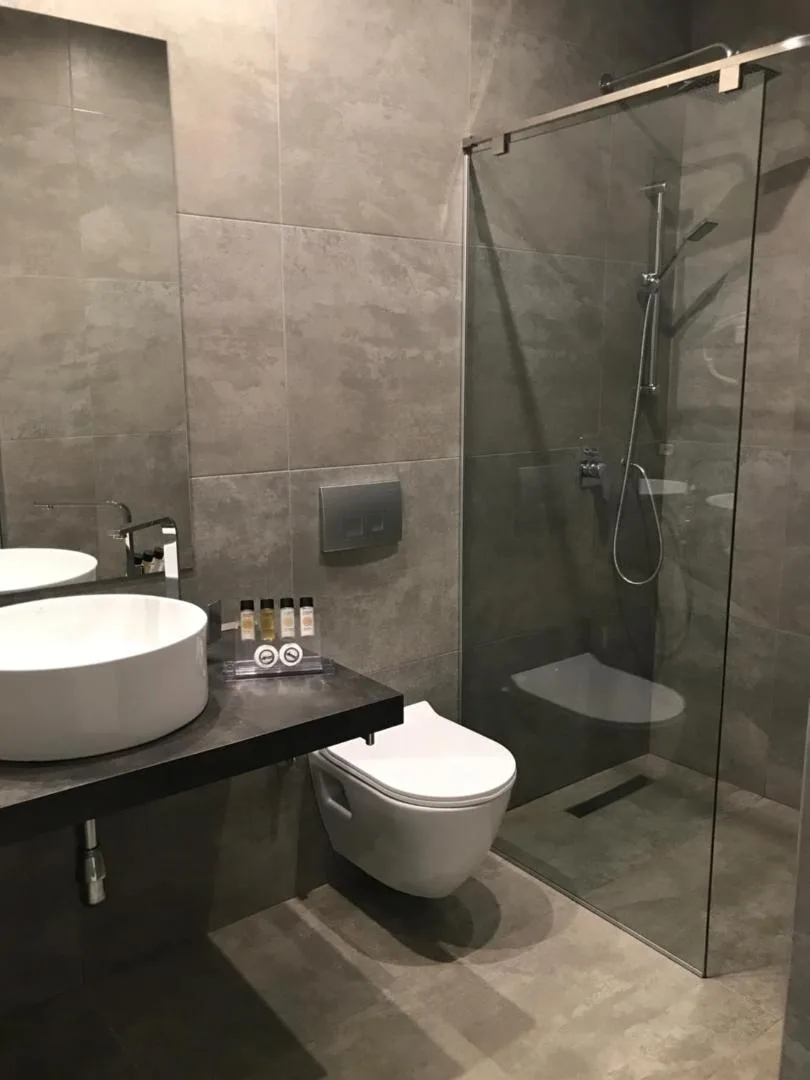 A grey-tiled bathroom with a walk-in glass shower, a wall-hung toilet and a vessel basin