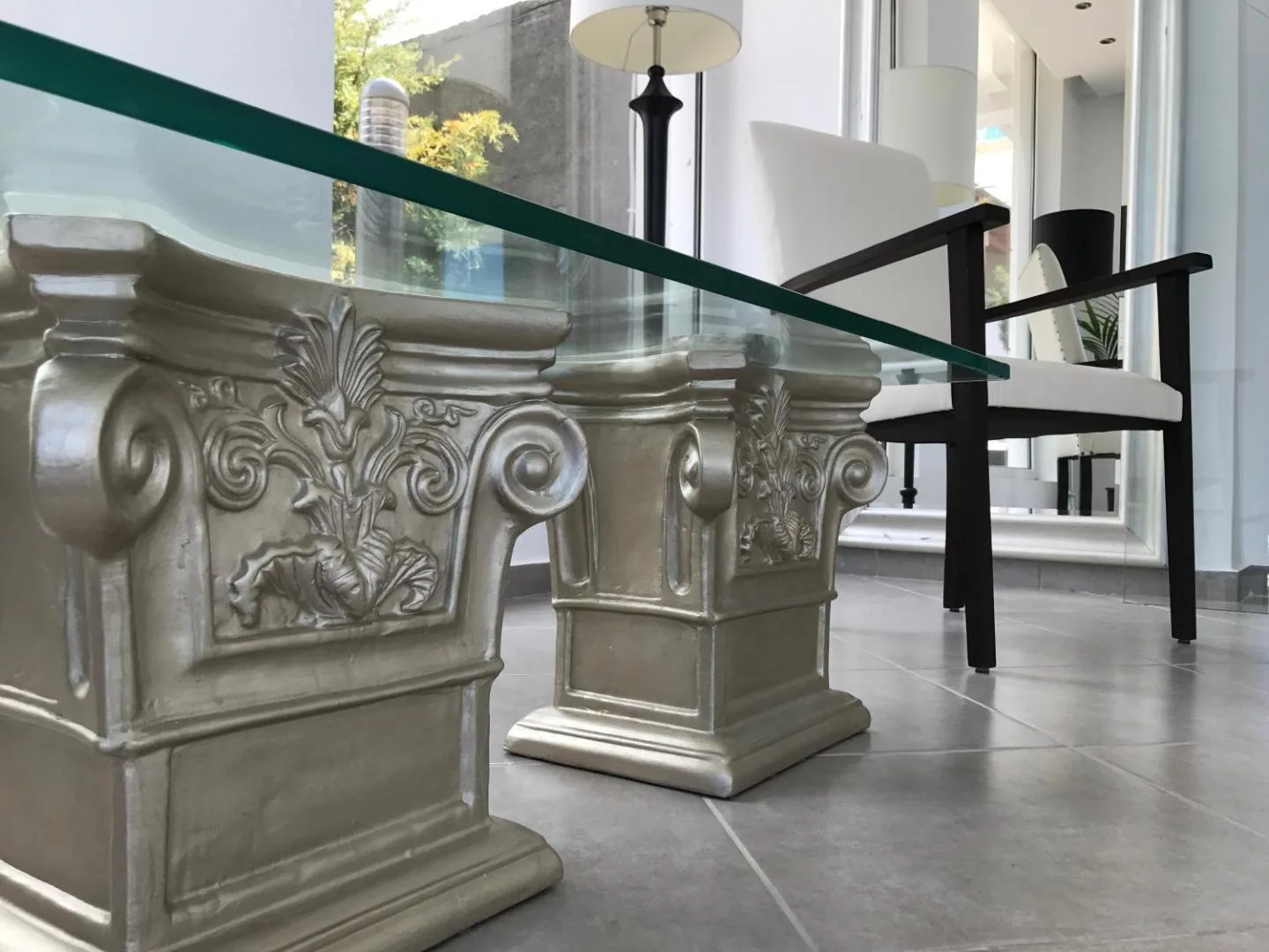 A glass table top on silver Corinthian capitals, a dark chair beside it
