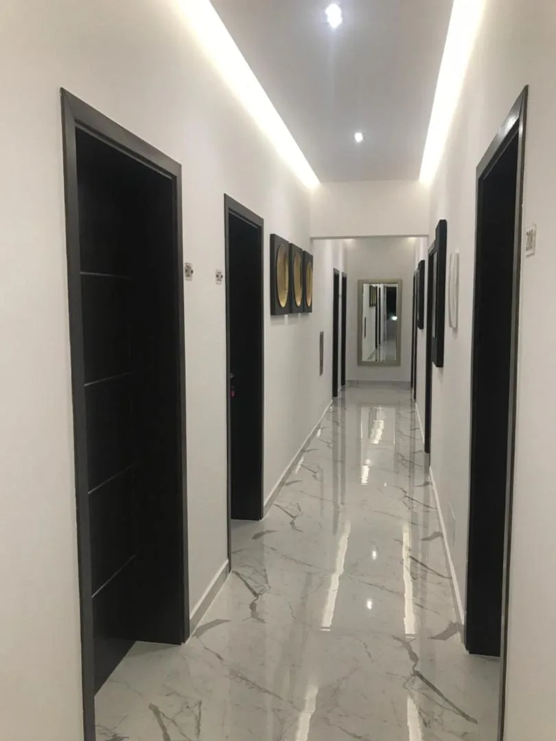 A long white corridor with a polished marble floor and dark room doors