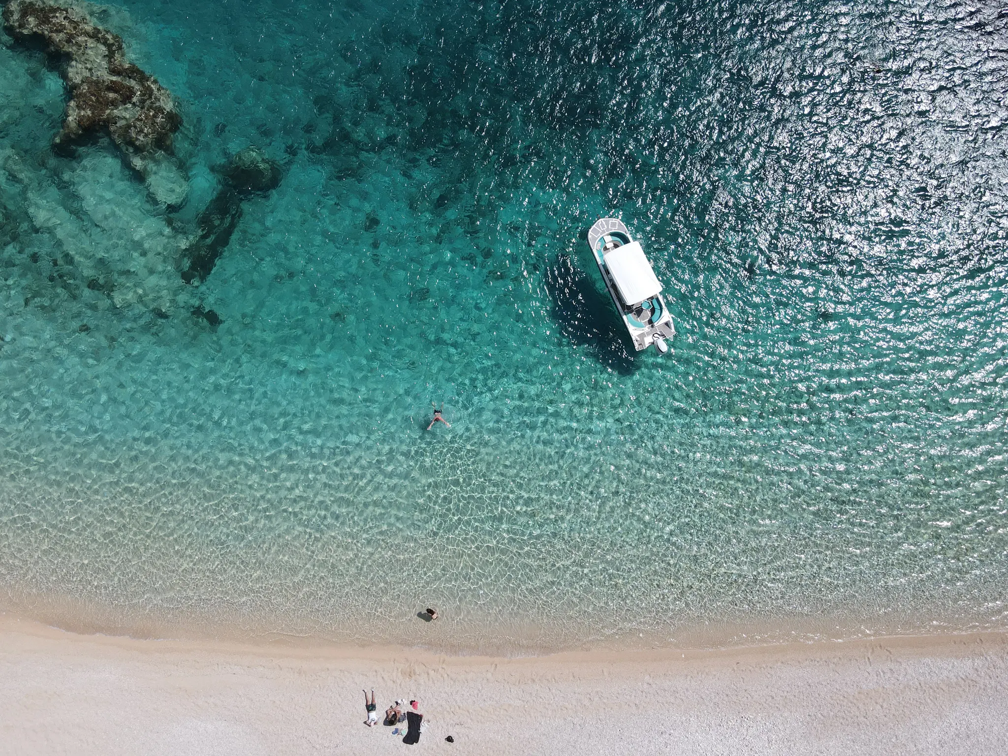 Gjipe from directly above: pale sand, a boat at anchor and swimmers in clear turquoise water