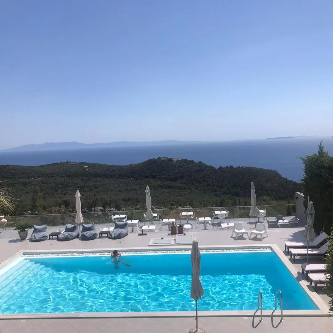 The pool and its loungers from above, the wooded hillside dropping away and islands on the horizon