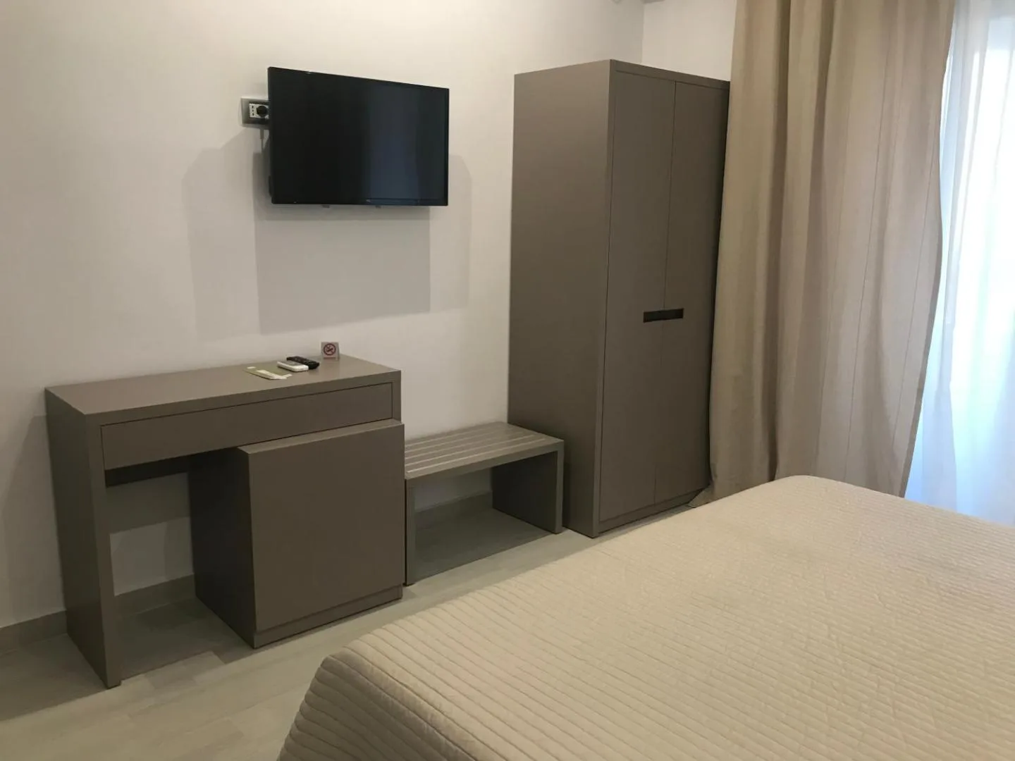 The other side of a room: a wall-mounted TV over a grey desk and a tall grey wardrobe