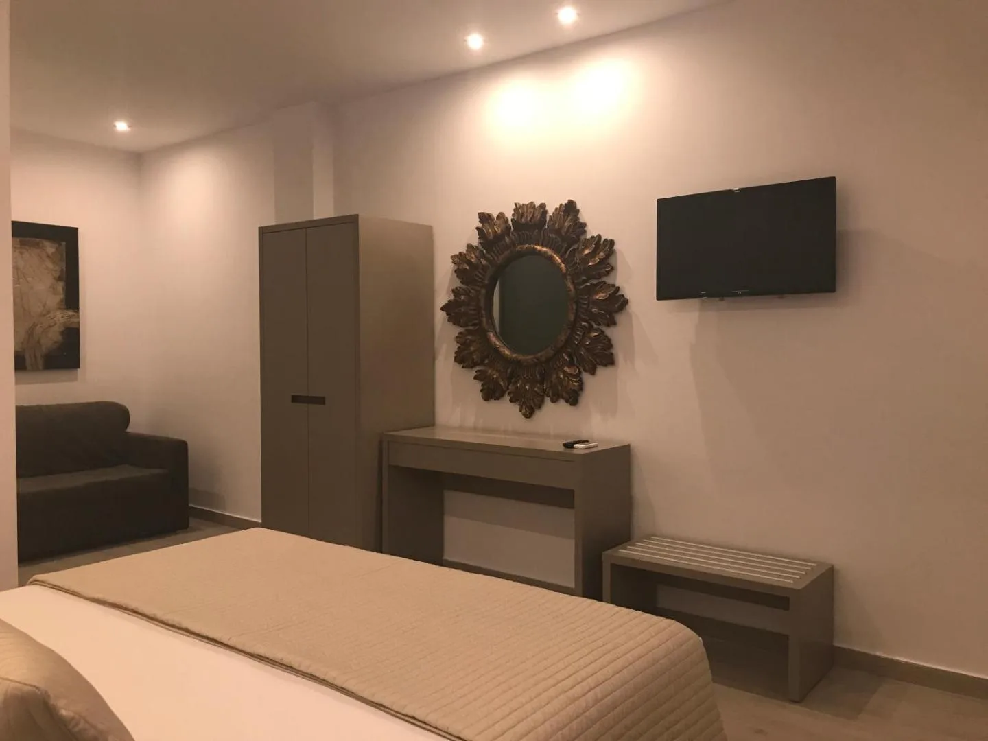 A double room with a gilt sunburst mirror on the wall, a TV, a desk and a wardrobe