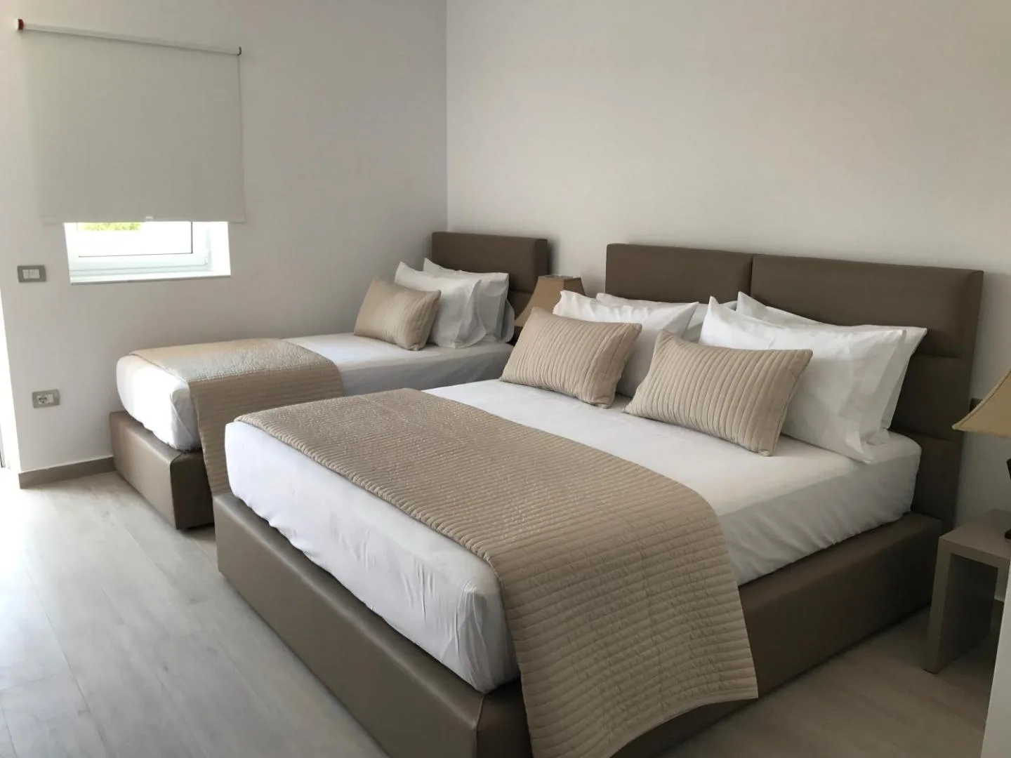 A room with a double bed and a single bed side by side, beige bedspreads and cushions
