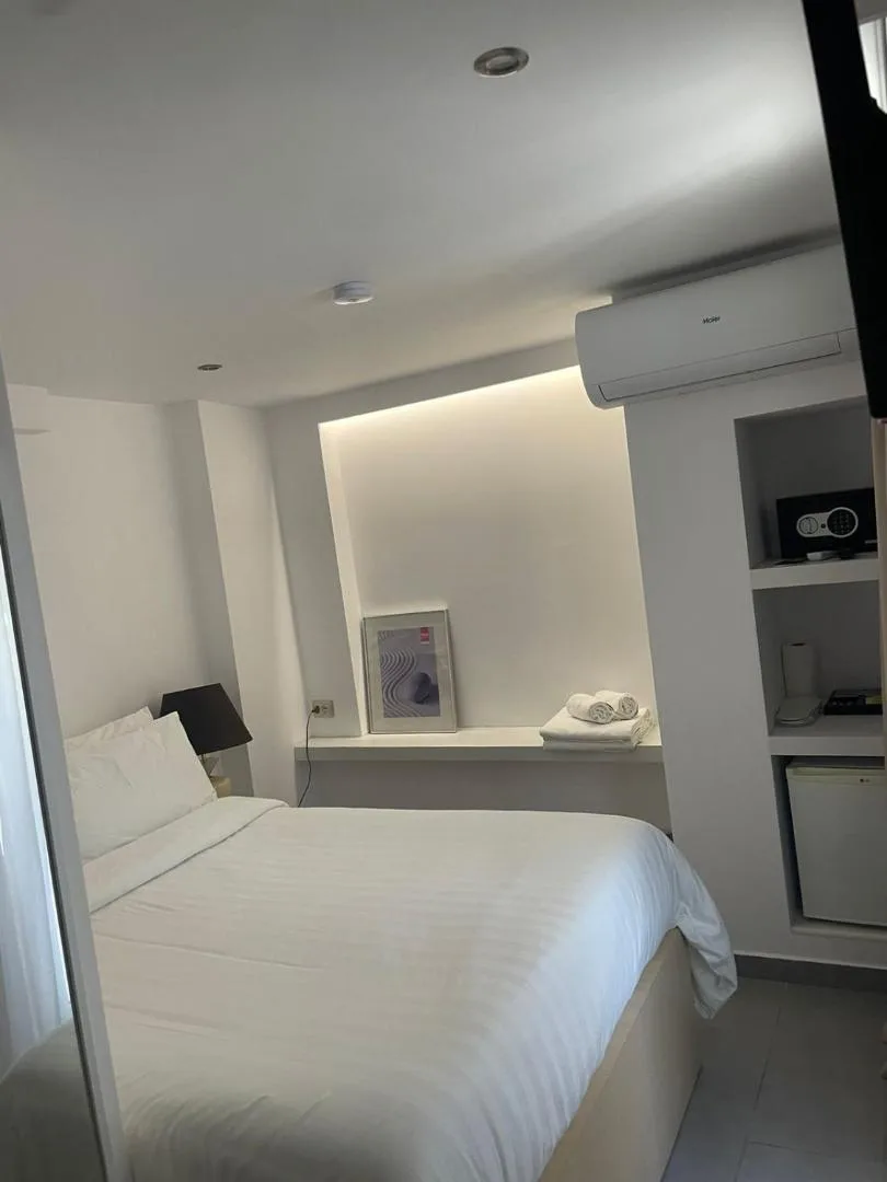 A compact white room with a double bed and a lit niche of shelves beside it