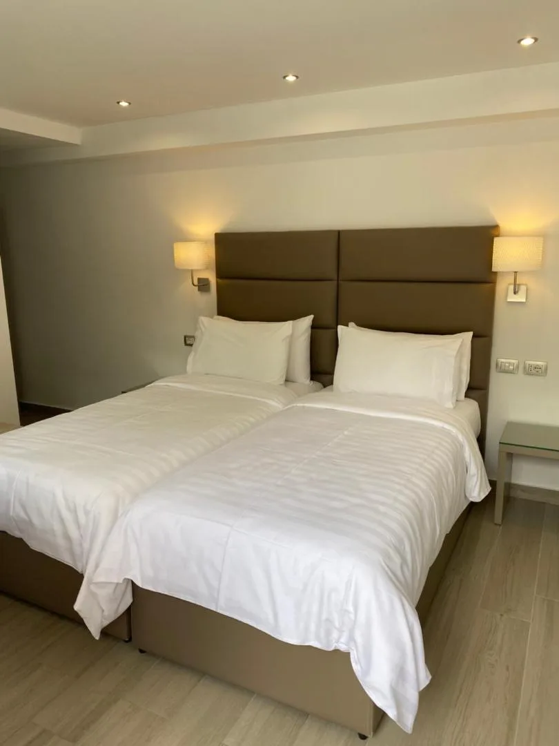 A twin room with two made-up single beds against a padded headboard and two bedside lamps