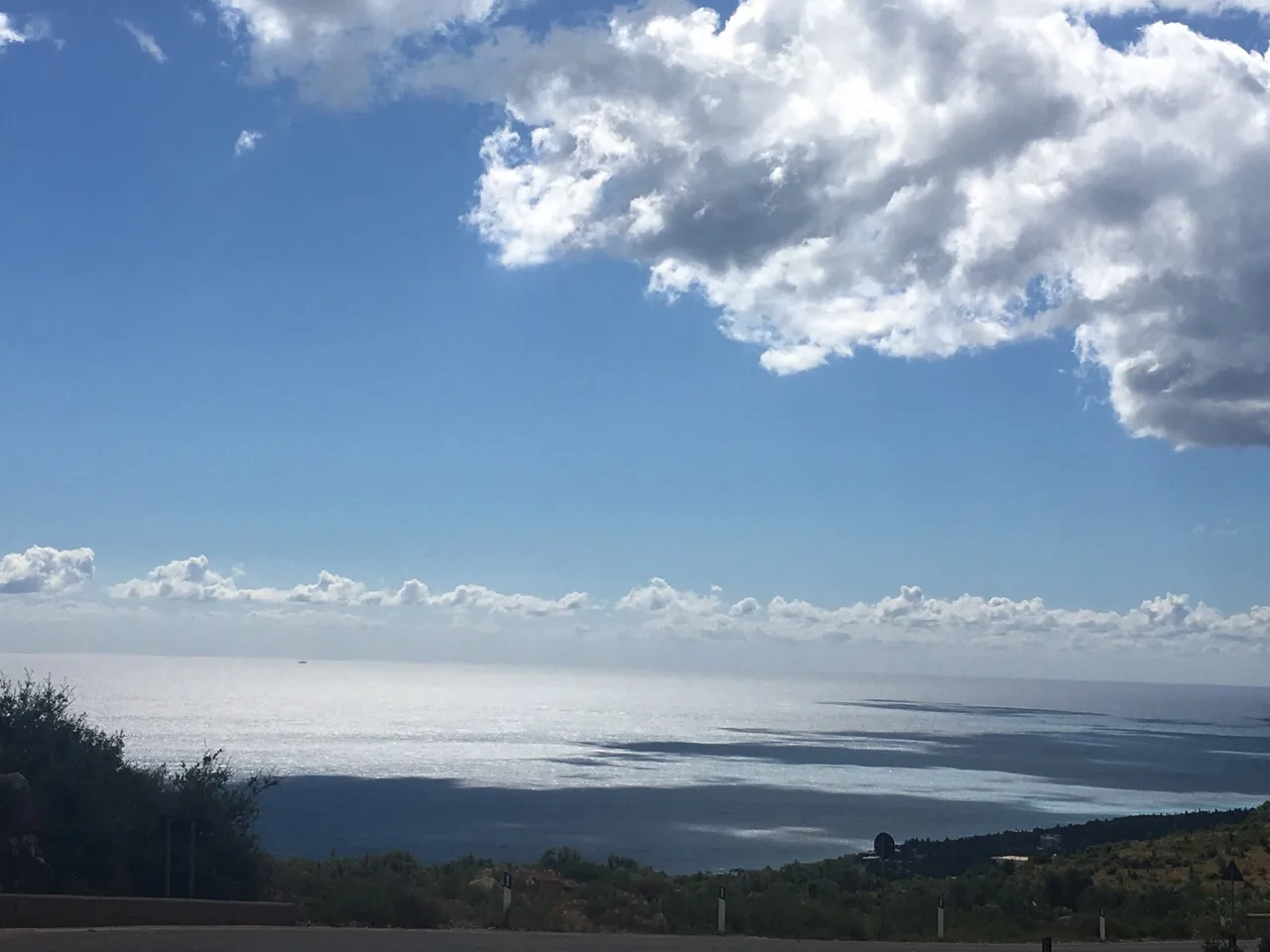 The sea from the hillside: a bright band of light on the water under a large cloud, the coast falling away below