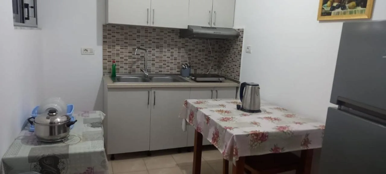 The ground-floor apartment's kitchen with a sink, hob, kettle, tall refrigerator and a table