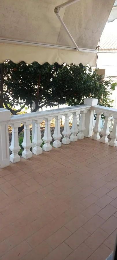 The ground-floor balcony's tiled floor and white balustrade under an awning, with a tree beyond