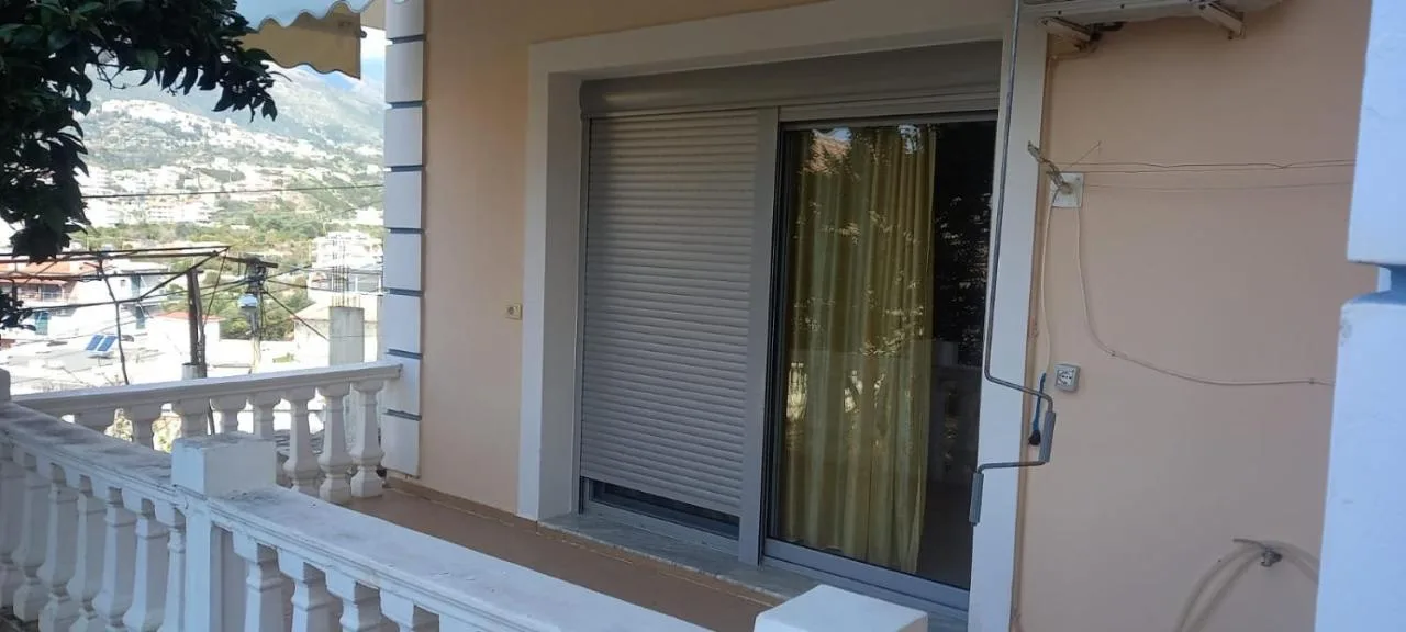 Sliding doors from the ground-floor apartment onto its balcony behind a white balustrade, with the hill beyond