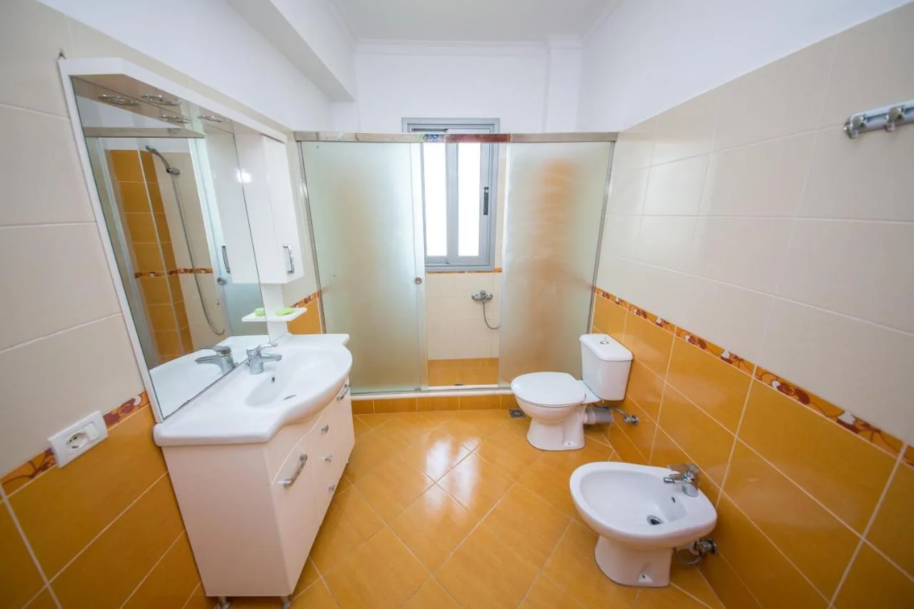 A bathroom with orange and white tiles, a glass shower, a basin unit and a bidet