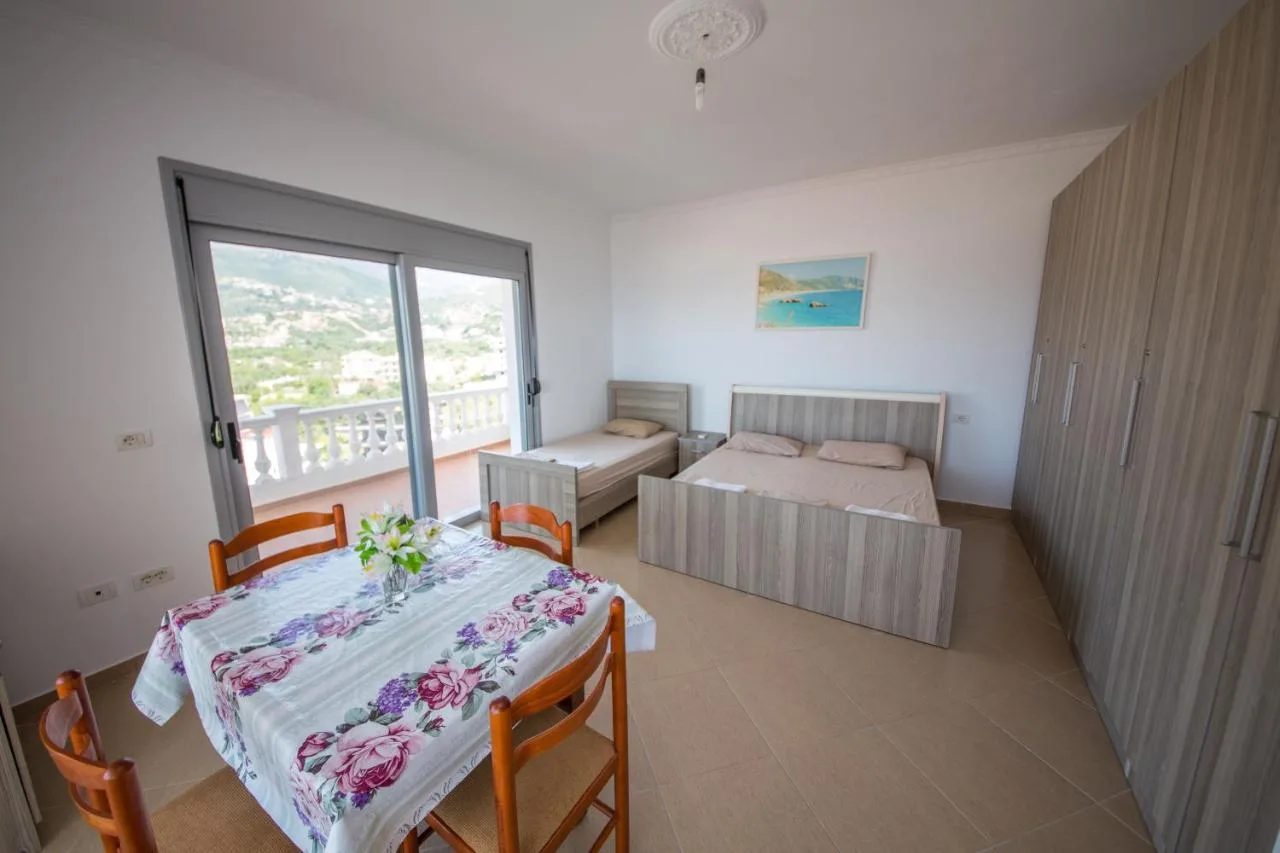A double and a single bed beside glass doors onto a balustraded balcony, with a dining table in front