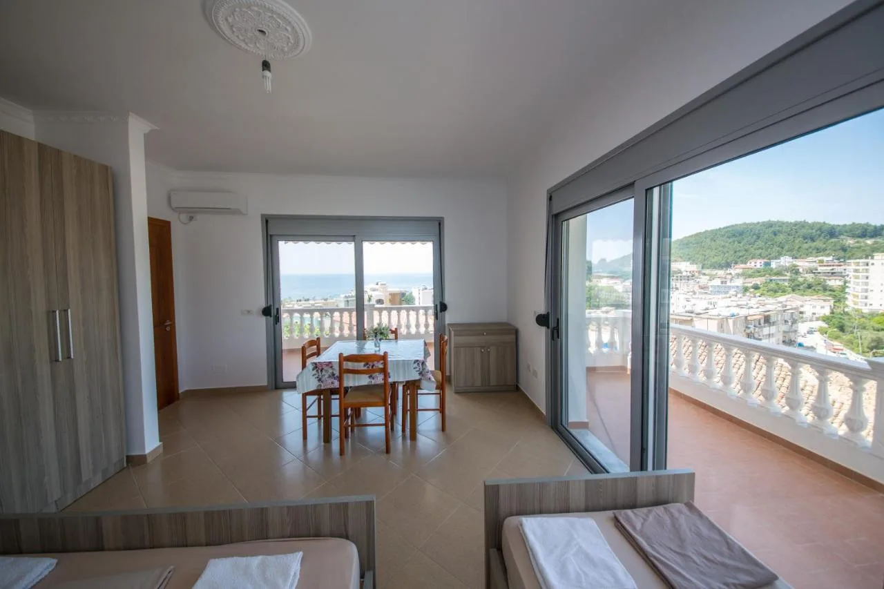 A bright living room with a dining table, two single beds and a wall of glass onto the balcony and the bay