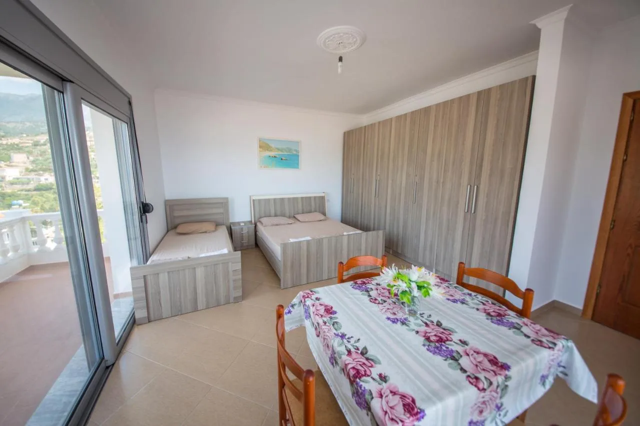 Two beds, a tall wardrobe and a table with a floral cloth beside the glass balcony doors