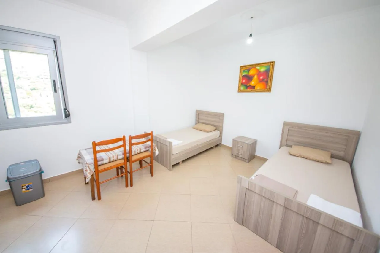Two single beds, a small table and chairs in a white room with a window
