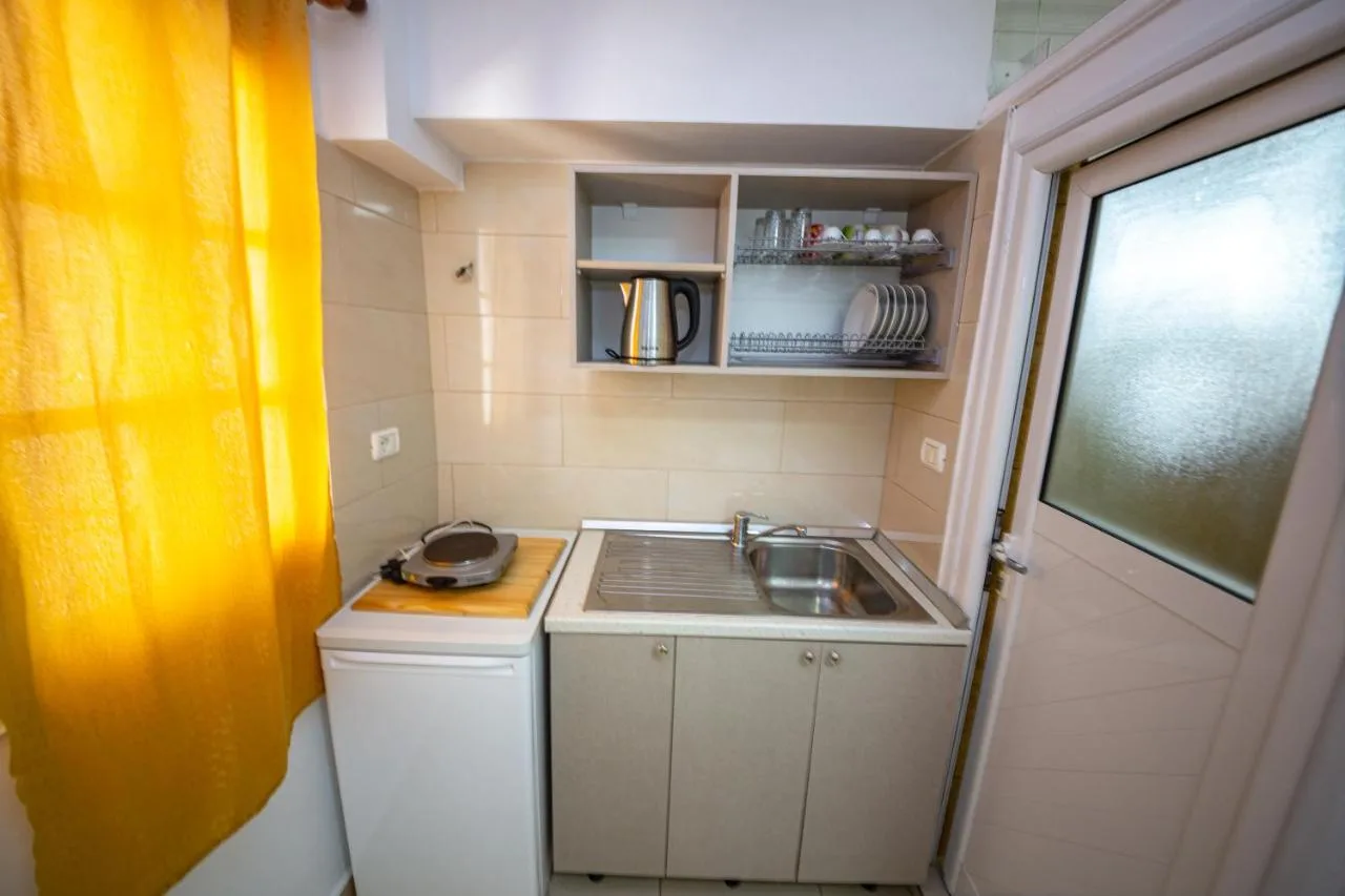 A studio kitchenette with a hob, sink, kettle and open shelves beside a yellow curtain