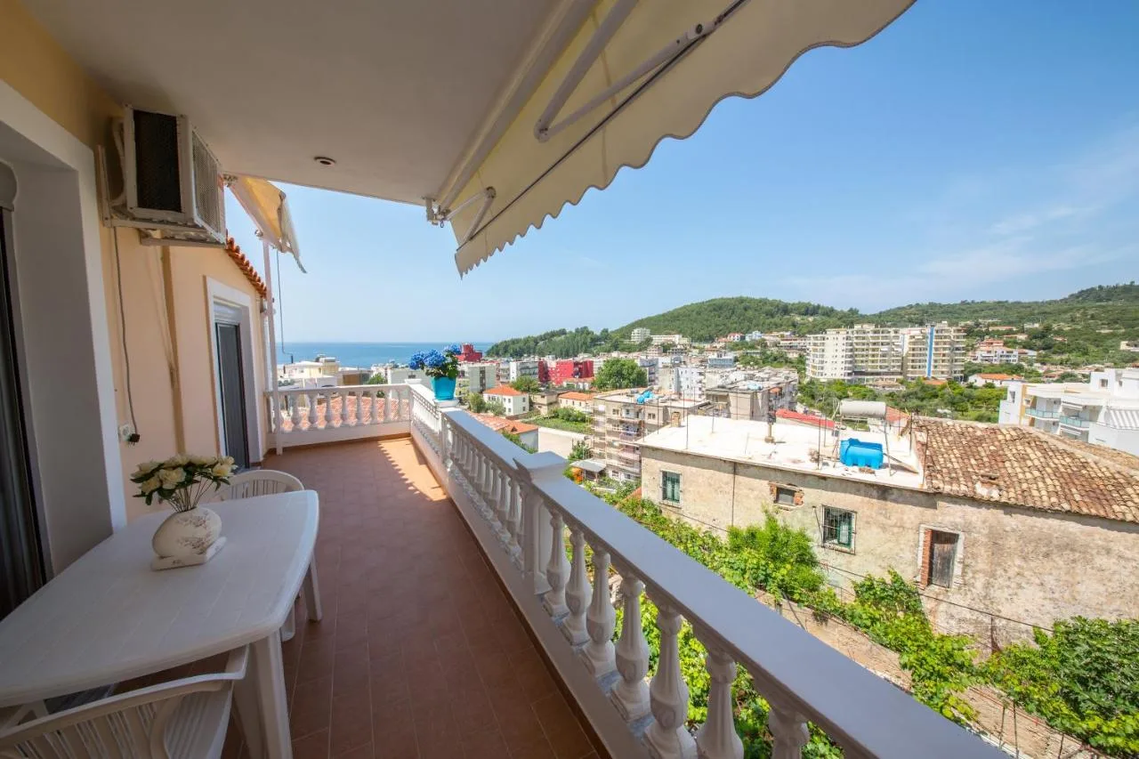 A long tiled terrace with a white balustrade, a table under the awning, and the view over Spile's roofs to the sea