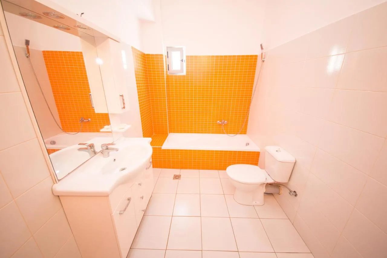 A bathroom with orange tiles, a bathtub, a basin unit and a large mirror