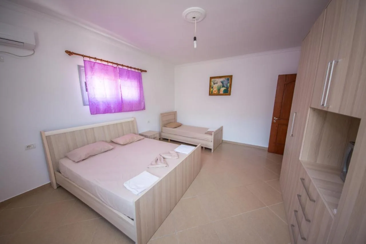 A bedroom with a double bed and a single bed, a wardrobe and a violet curtain