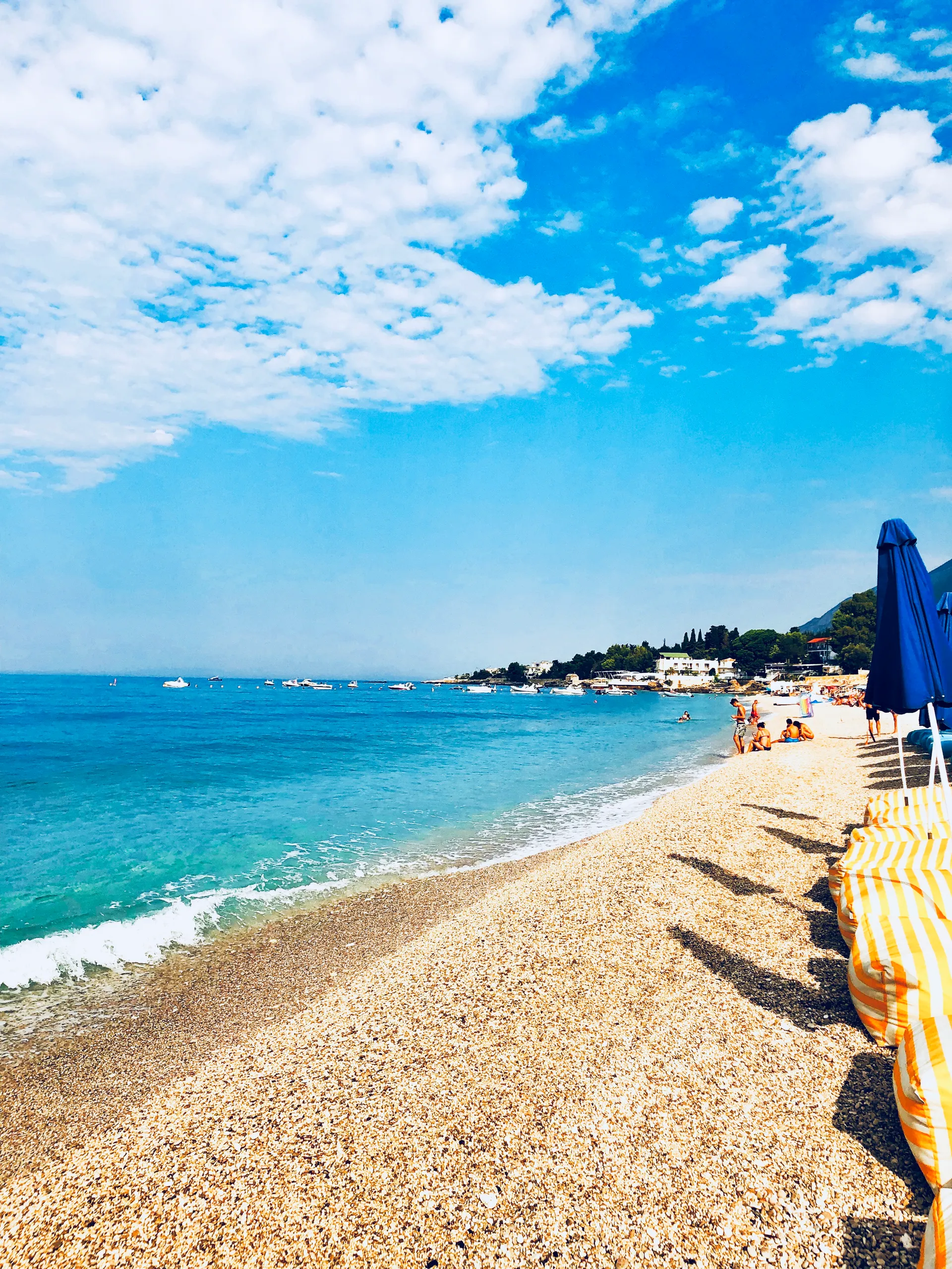 Dhërmi beach in summer: turquoise water over white pebble curving towards the headland