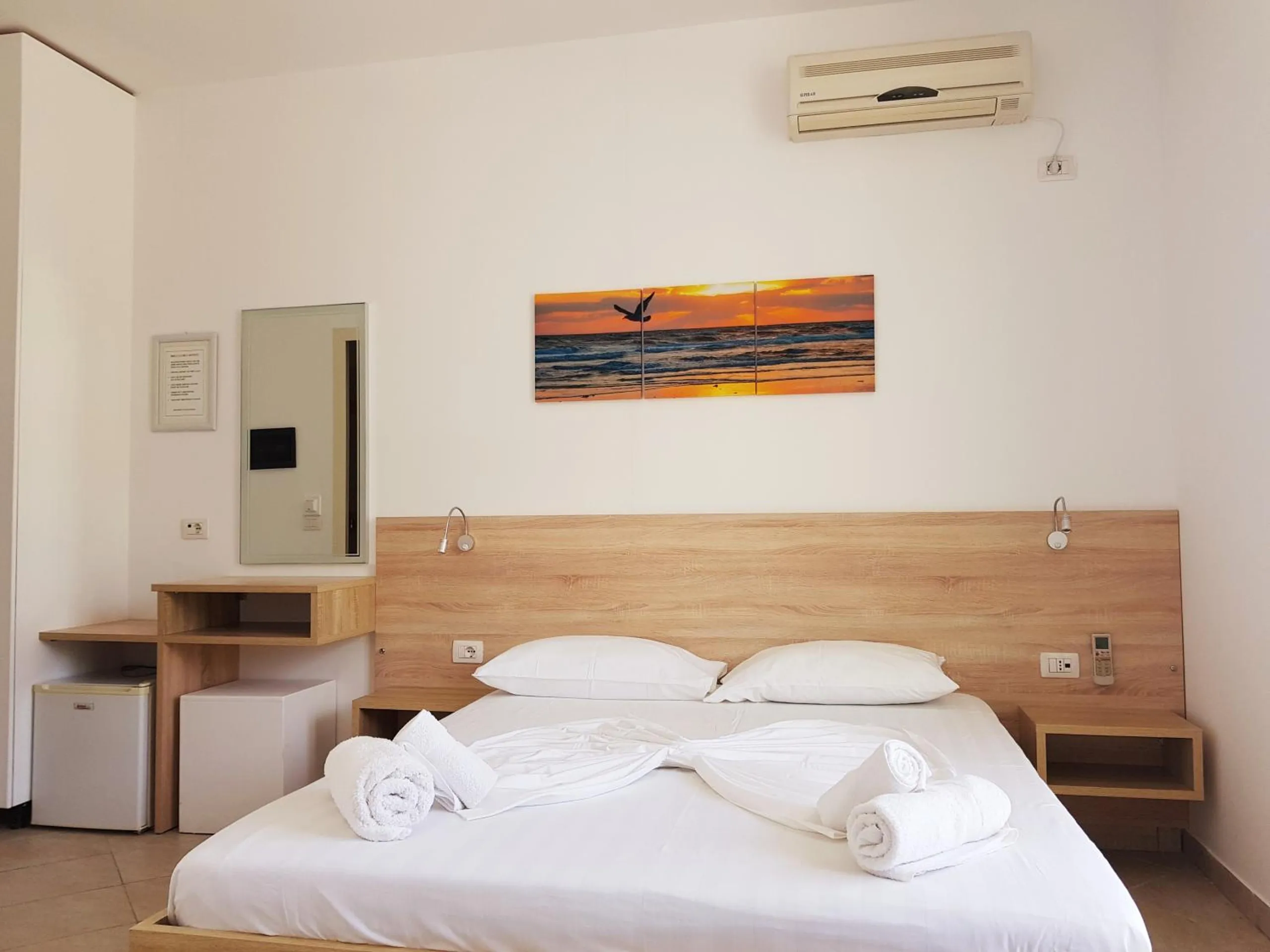 A double room with a sunset print above the bed, a dressing table and a small fridge