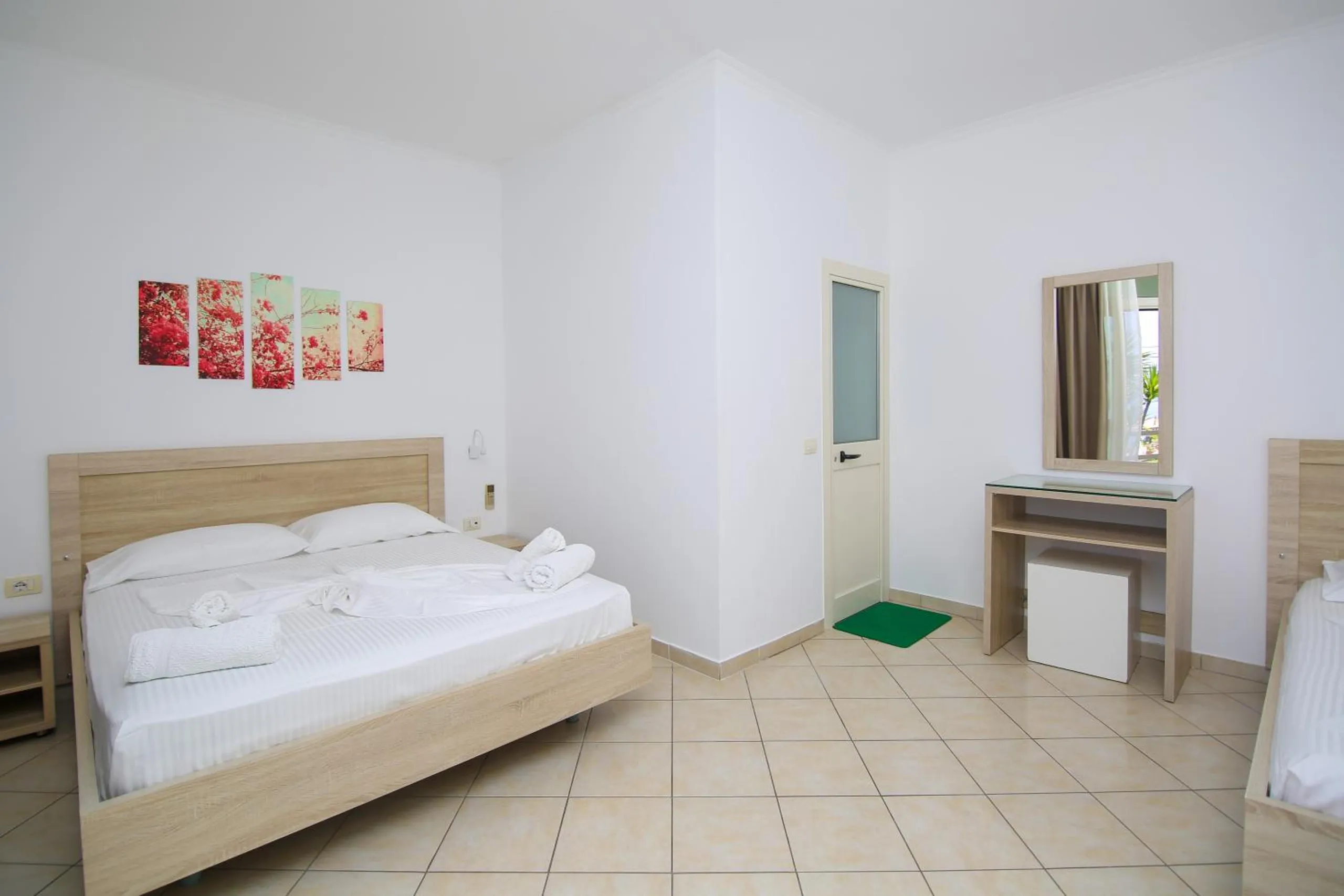 A triple room with a double bed and a single bed, a dressing table and mirror, beige tiled floor