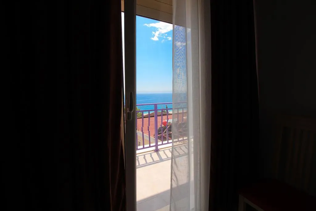 A dim room at Hotel Keisa with the balcony door open on a bright strip of blue sea and sky