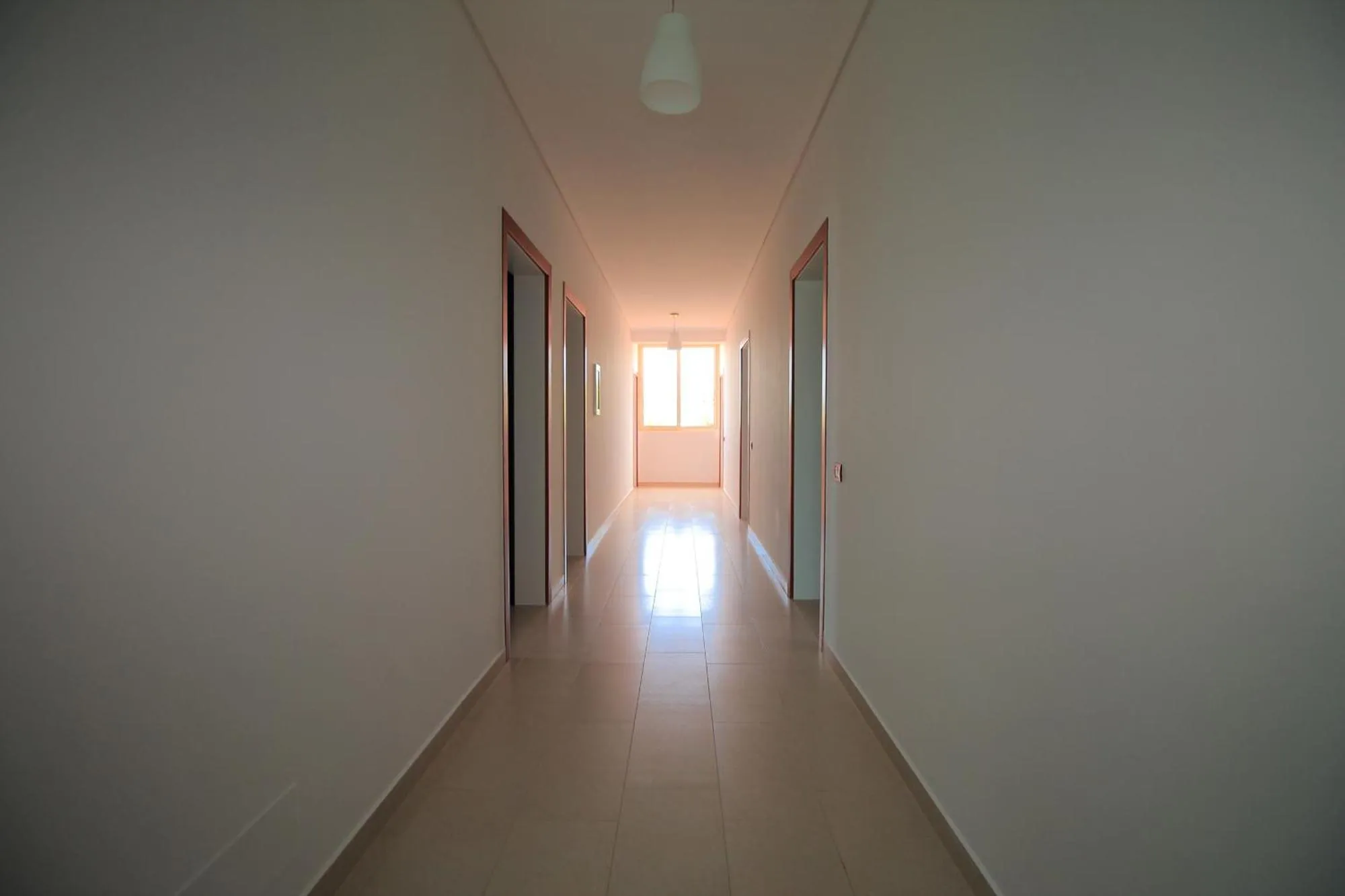 A long white corridor at Hotel Keisa with grey tiled floor and room doors along one side