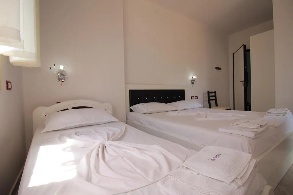 A room at Hotel Keisa with a single bed by the window and a double bed with a black headboard, towels folded on the white covers