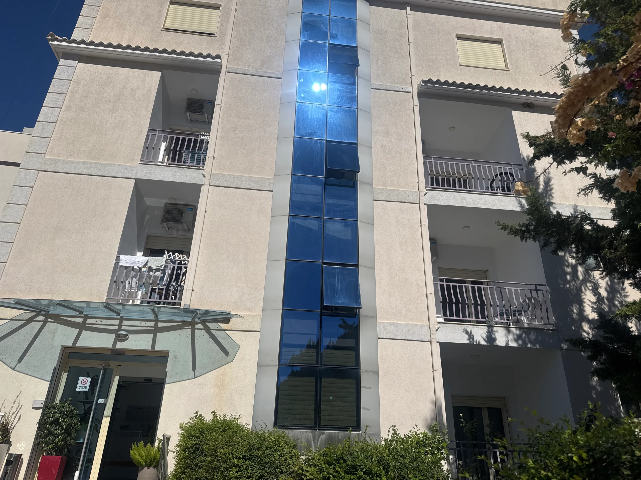 The cream front of Hotel Keisa with its balconies, the glass stair column running up the middle, the fan-shaped glass canopy over the door and a clipped hedge along the front