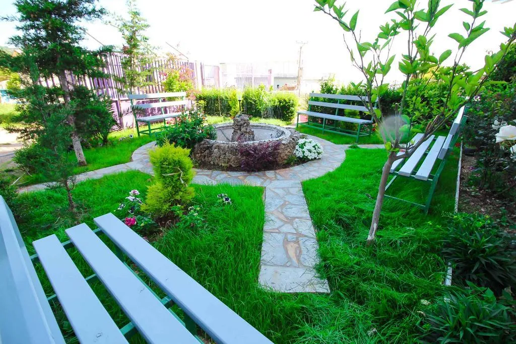 A stone path through the lawn of the front garden at Hotel Keisa, with white benches and young trees
