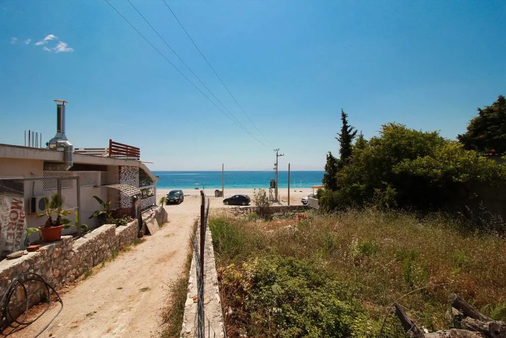 A dirt lane running down between a stone wall and scrub to parked cars and the sea at Dhërmi beach