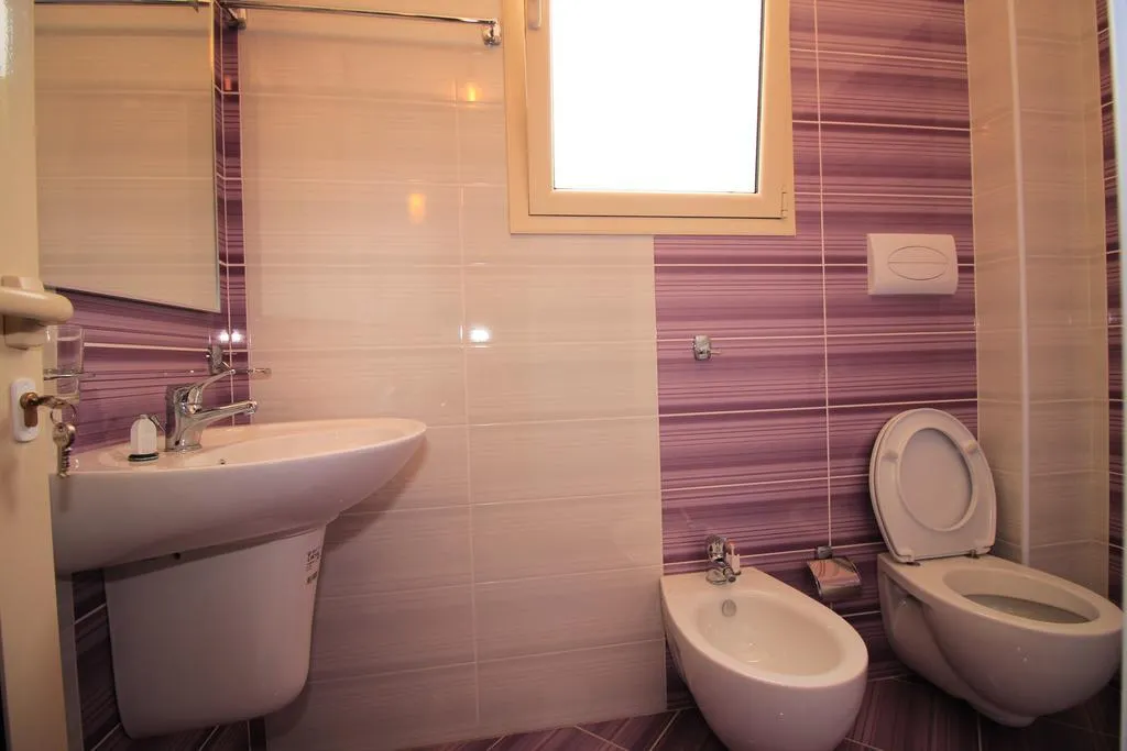 A shower room at Hotel Keisa tiled in lilac and white, with a basin, a toilet and a bidet